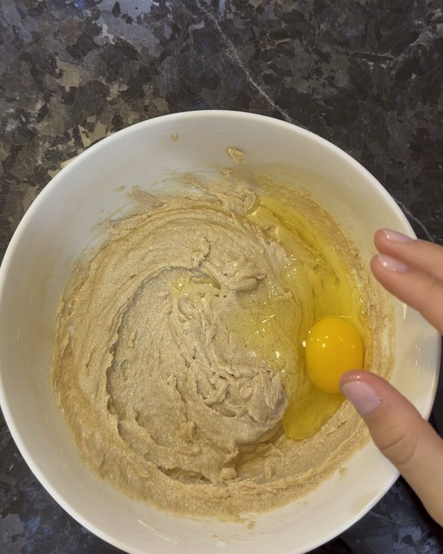 An egg added to creamed butter and sugar in a white bowl
